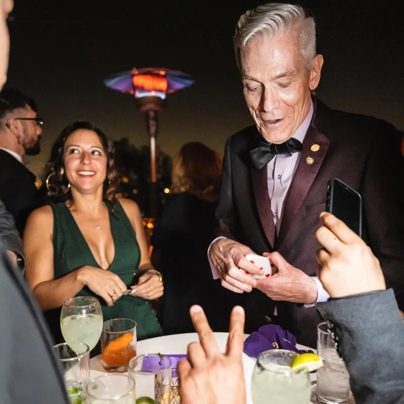 Felix Jones performing close-up card magic for delighted guests at an evening cocktail reception