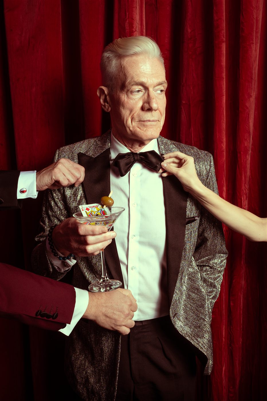 Felix Jones having his bow tie adjusted while holding a martini glass with a playing card